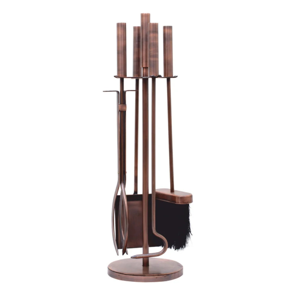 A traditional four-piece Stamford fireside companion set featuring log tongs, a fire poker, an ash shovel, and a hearth brush neatly hung on a freestanding circular base stand in a hand-finished antique copper style.