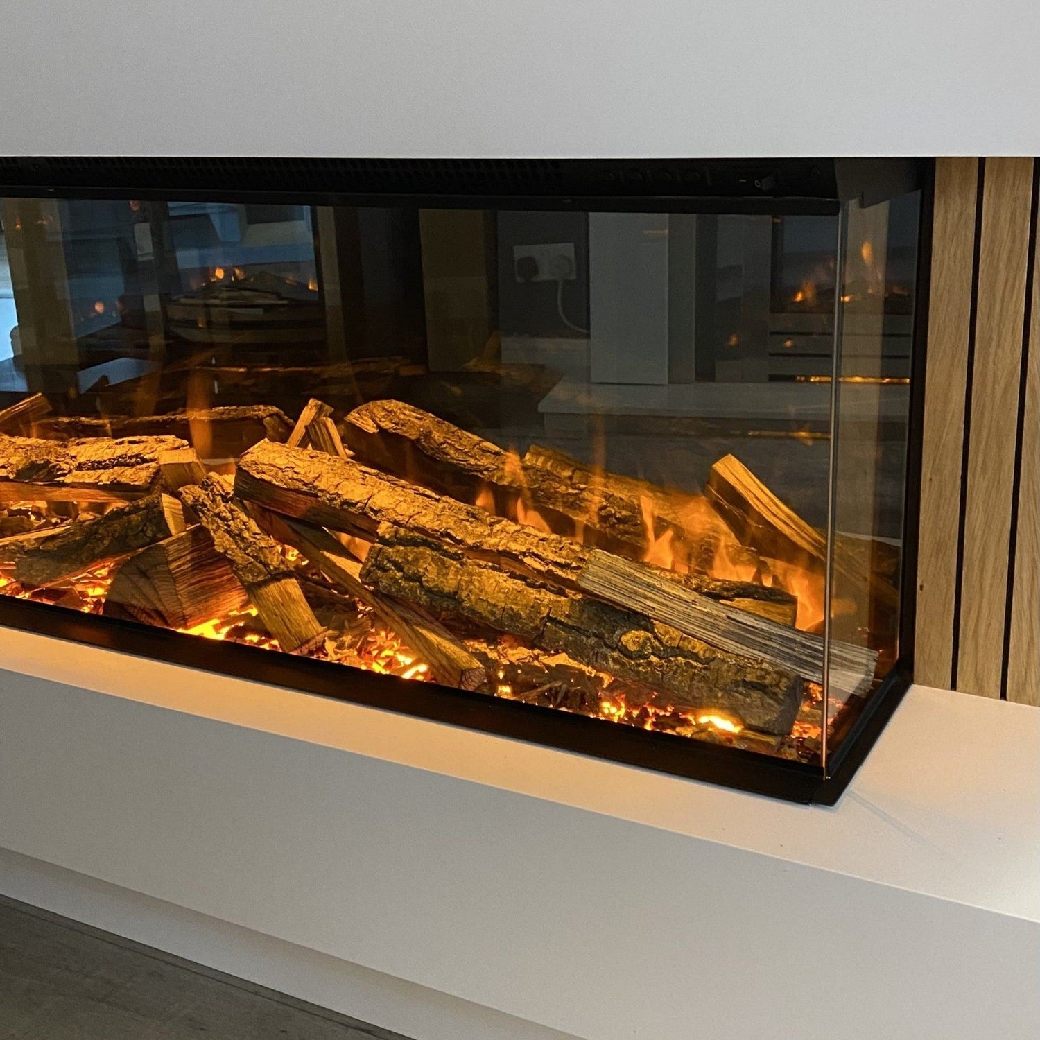 Panoramic 3-sided electric media wall fire with realistic glowing log fuel bed and vertical oak slat panel accents.