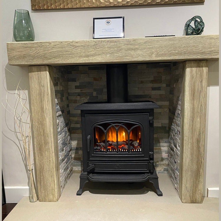 Traditional black electric stove log burner with realistic glowing flame effect inside a rustic oak beam fireplace surround.