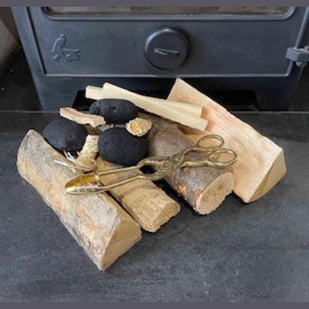 Brass coal tongs with leaf handles on hearth among firewood and stove