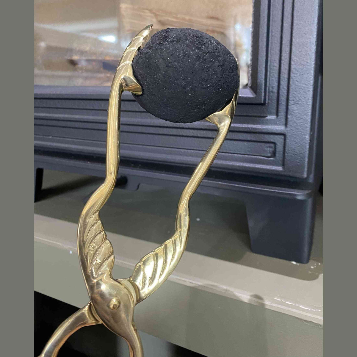 Close-up of brass coal tong gripping black coal lump near stove