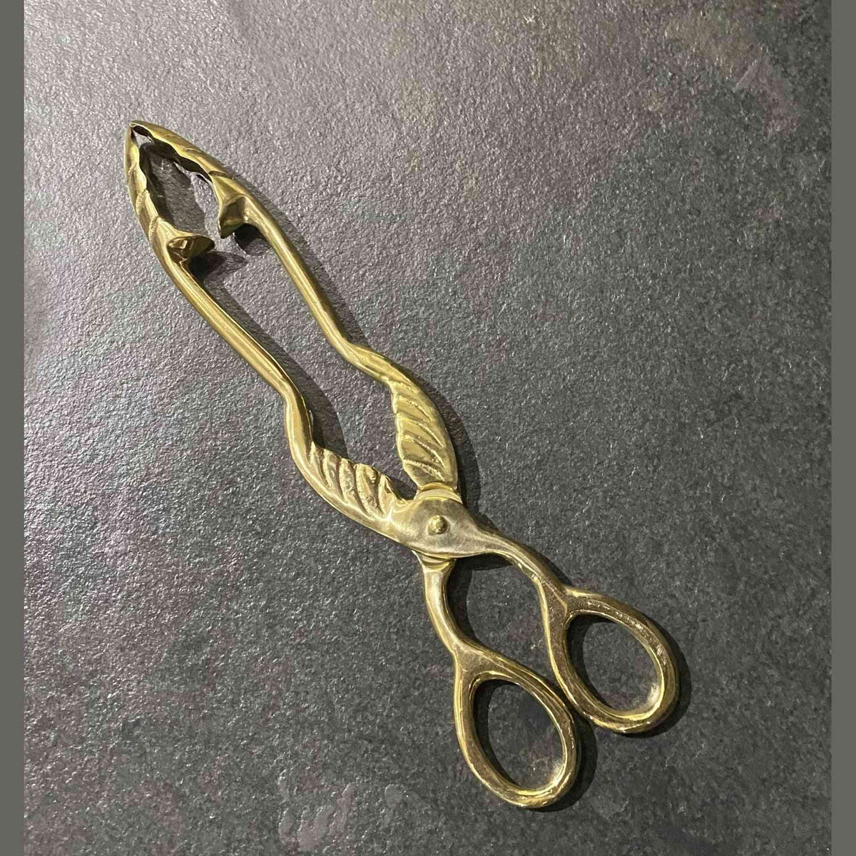 Top-down view of brass coal tongs showing oval loops and pivot