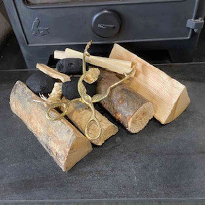 Ornate brass log burner tongs resting on split wood and coal