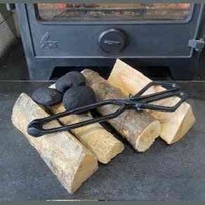 Open cast iron firewood tongs resting on split logs beside metal stove