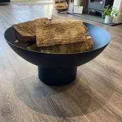 Black mild steel fire pit bowl with stacked logs on wood floor