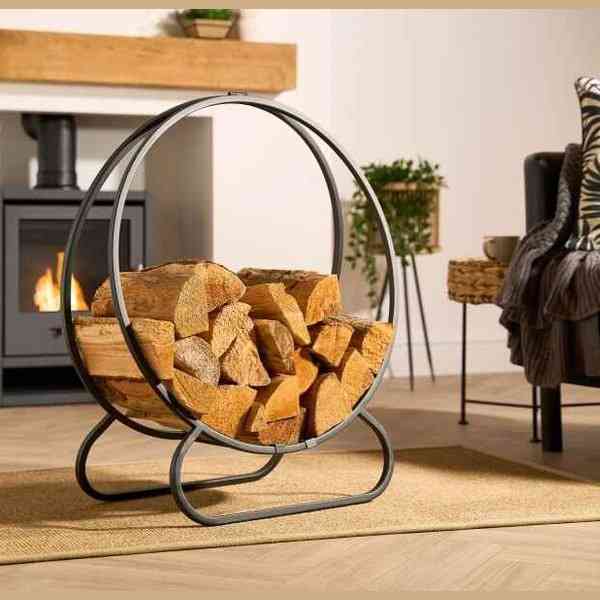 Black steel freestanding firewood log holder with circular frame beside wood stove