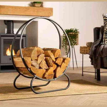 Black steel freestanding firewood log holder with circular frame beside wood stove