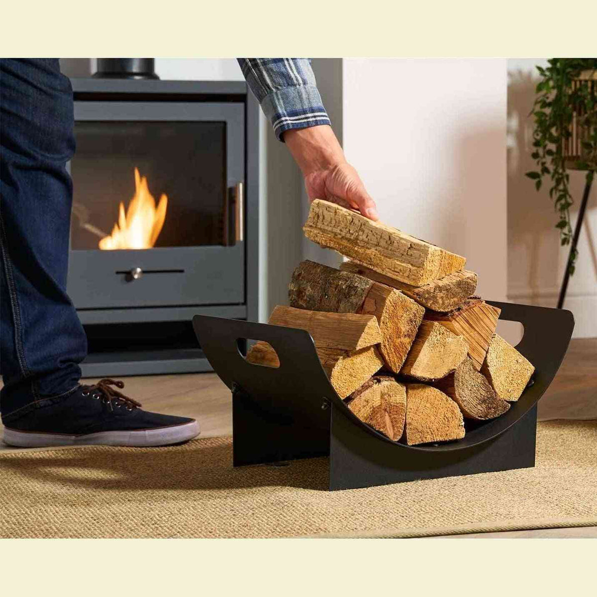 Person adding firewood to black industrial style log holder near active fireplace