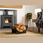 Black metal log rack holding firewood beside a lit wood-burning stove in a modern living room
