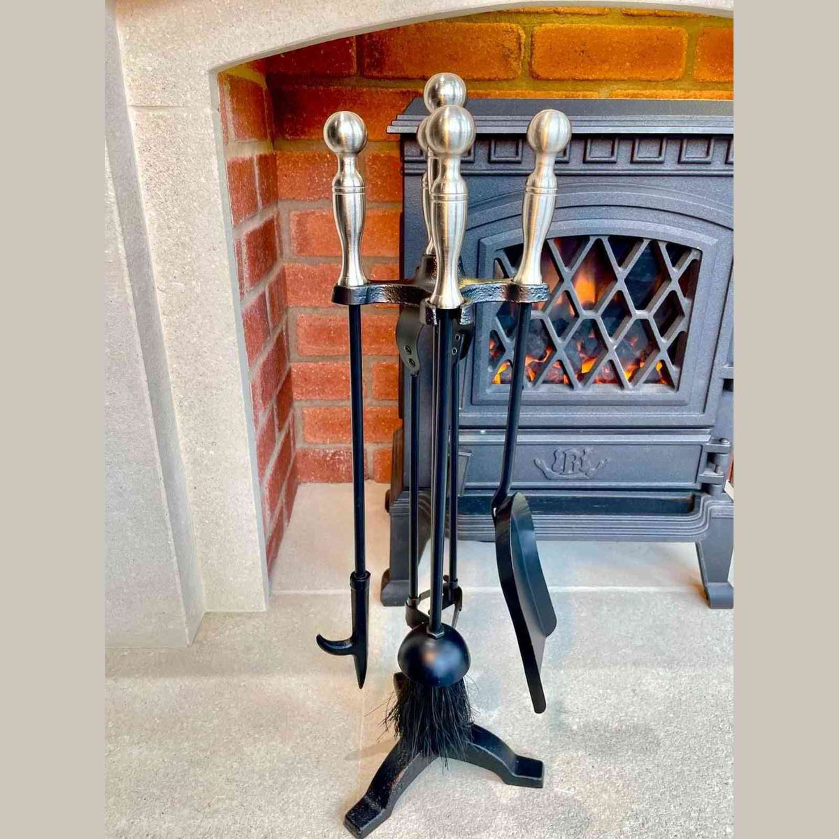 4-piece black metal fireplace tools with polished silver ball tops in tripod stand near brick hearth