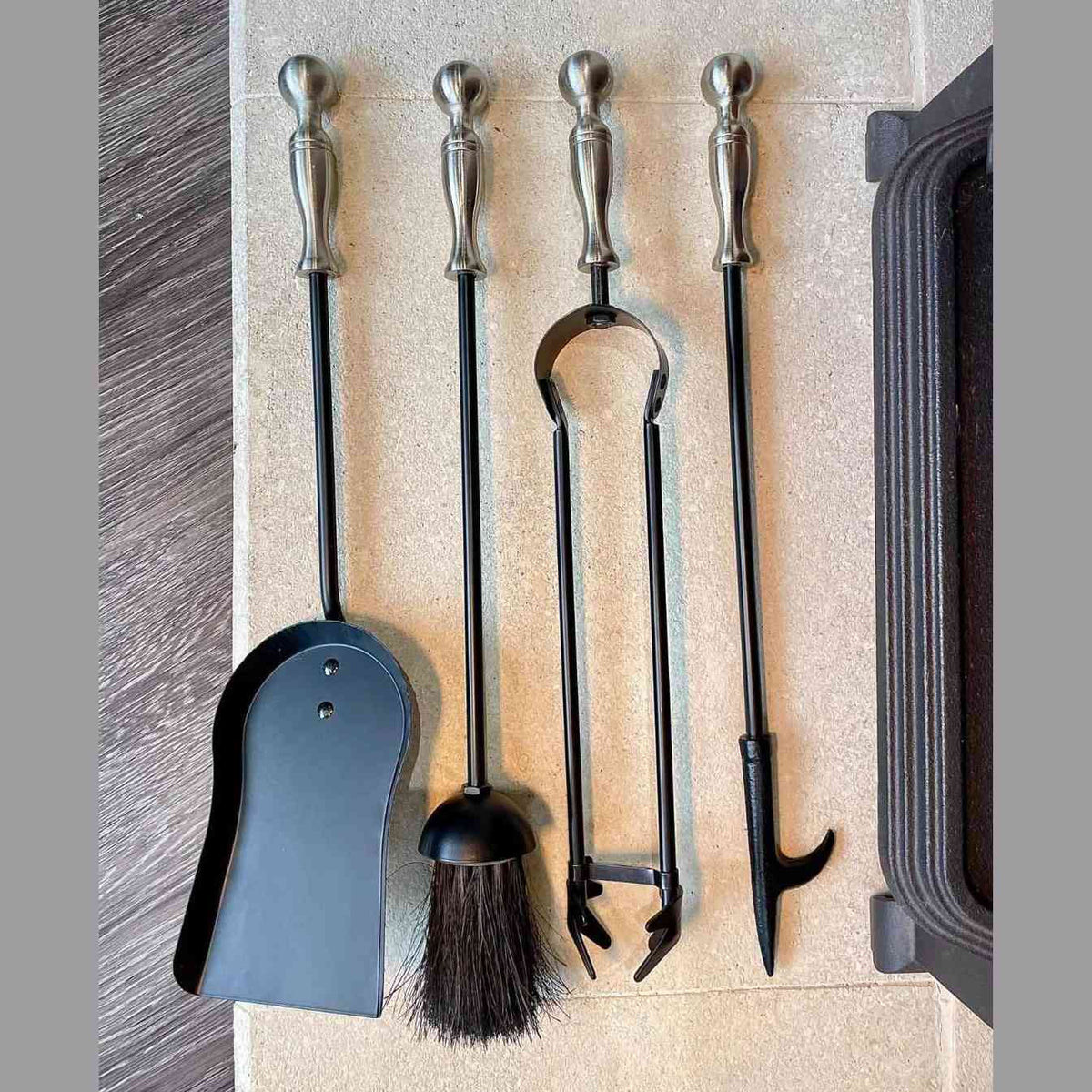 Black and pewter ball top fireplace tool set with dustpan, brush, tongs, and poker on stone hearth