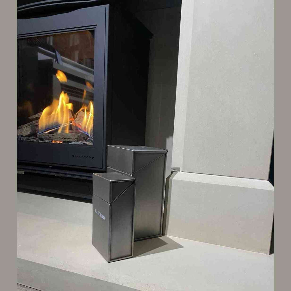 Brushed silver firelighter and matchbox holder set on stone hearth with lit stove