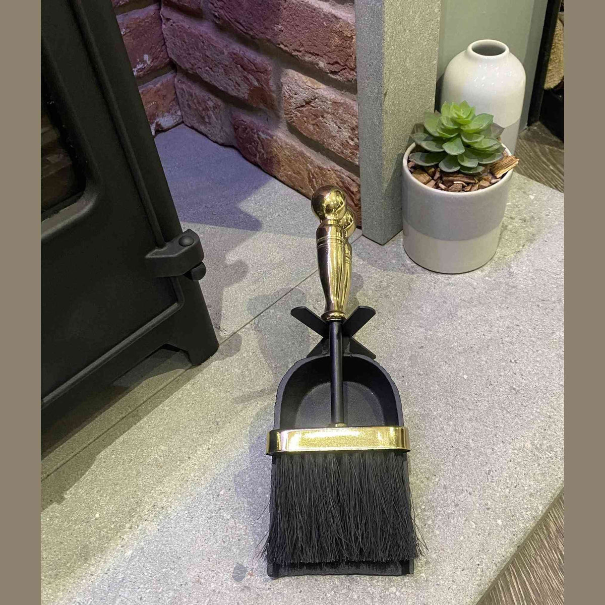 Black cast iron fireplace tool set with polished brass handles in stand near brick wall