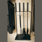 Black fireplace tool set with four long-handled tools including a poker, brush, tongs, and shovel on a black stand, modern hearth accessories.