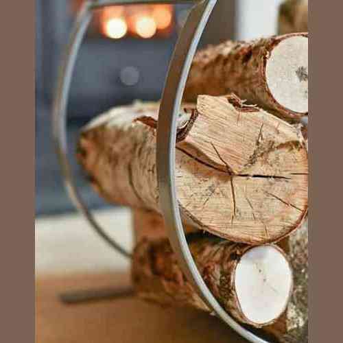 Forged steel fireplace log rack filled with birch logs near glowing fire