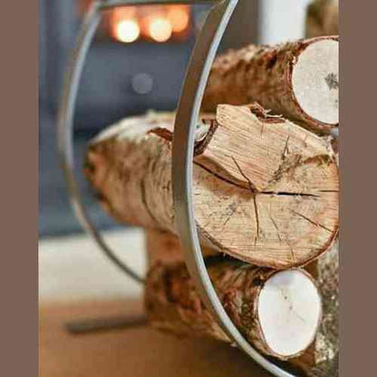 Forged steel fireplace log rack filled with birch logs near glowing fire