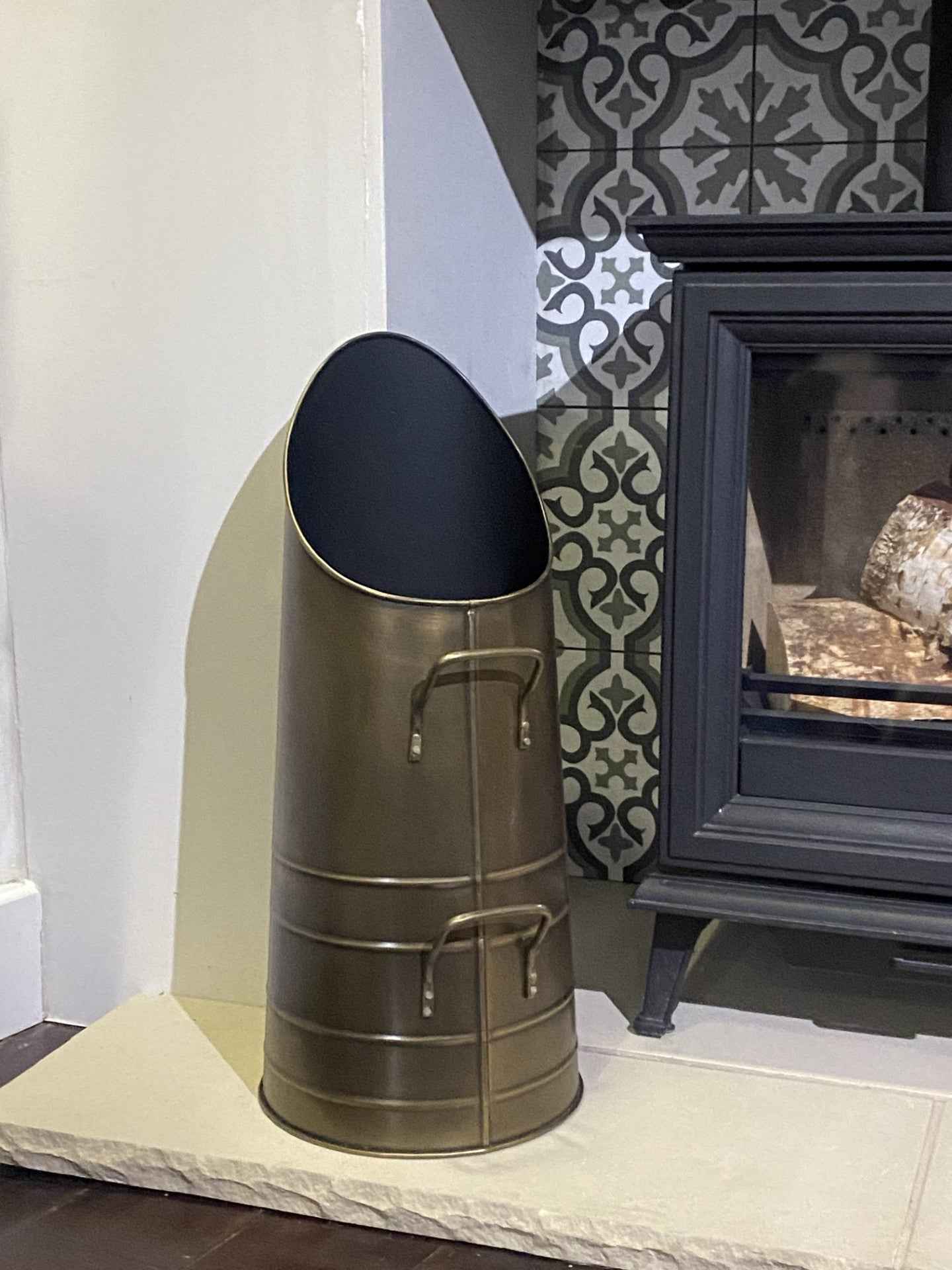  Close-up view of the 53.5cm Calfire Dryton antique hod coal bucket sitting on a light stone hearth next to a traditional fireplace stove.