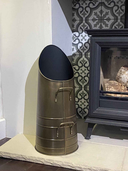  Close-up view of the 53.5cm Calfire Dryton antique hod coal bucket sitting on a light stone hearth next to a traditional fireplace stove.
