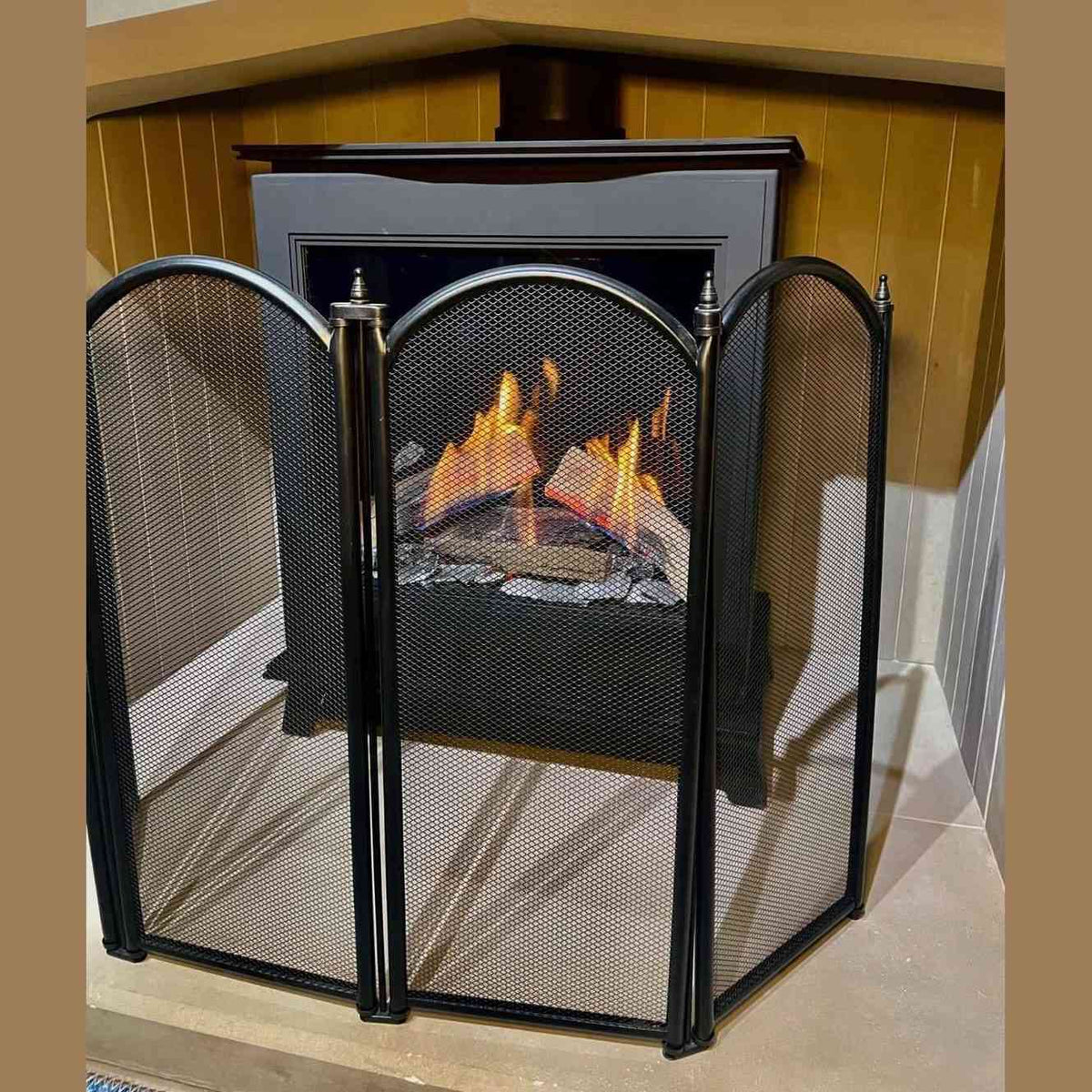Black steel fire guard screen forming semi-circular barrier around lit fireplace insert