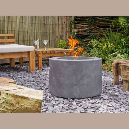 Field & Flame dark concrete grey portable fire pit in garden setting with wooden furniture and gravel ground
