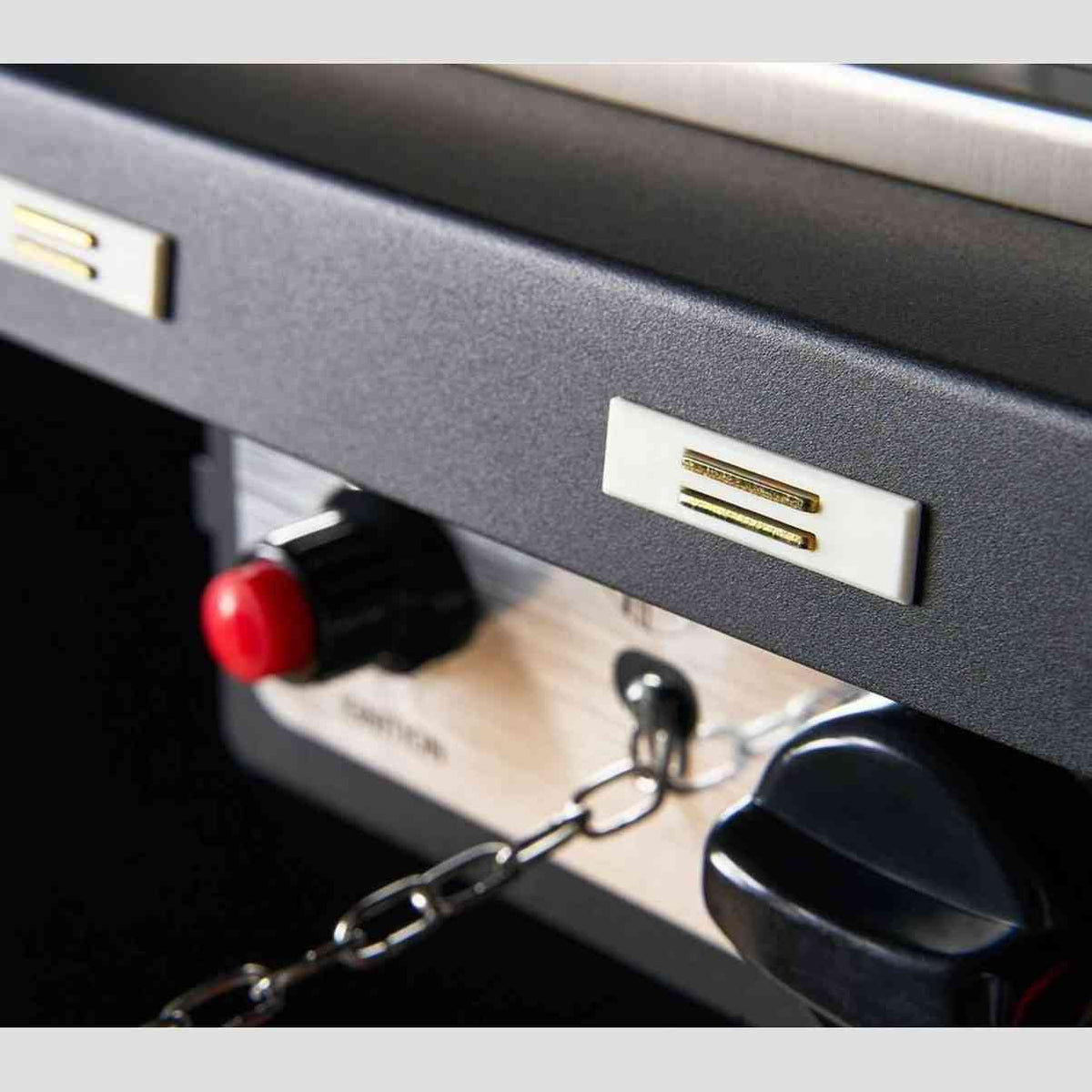 Detail of black textured metal side panel with gold accent bars and caution label