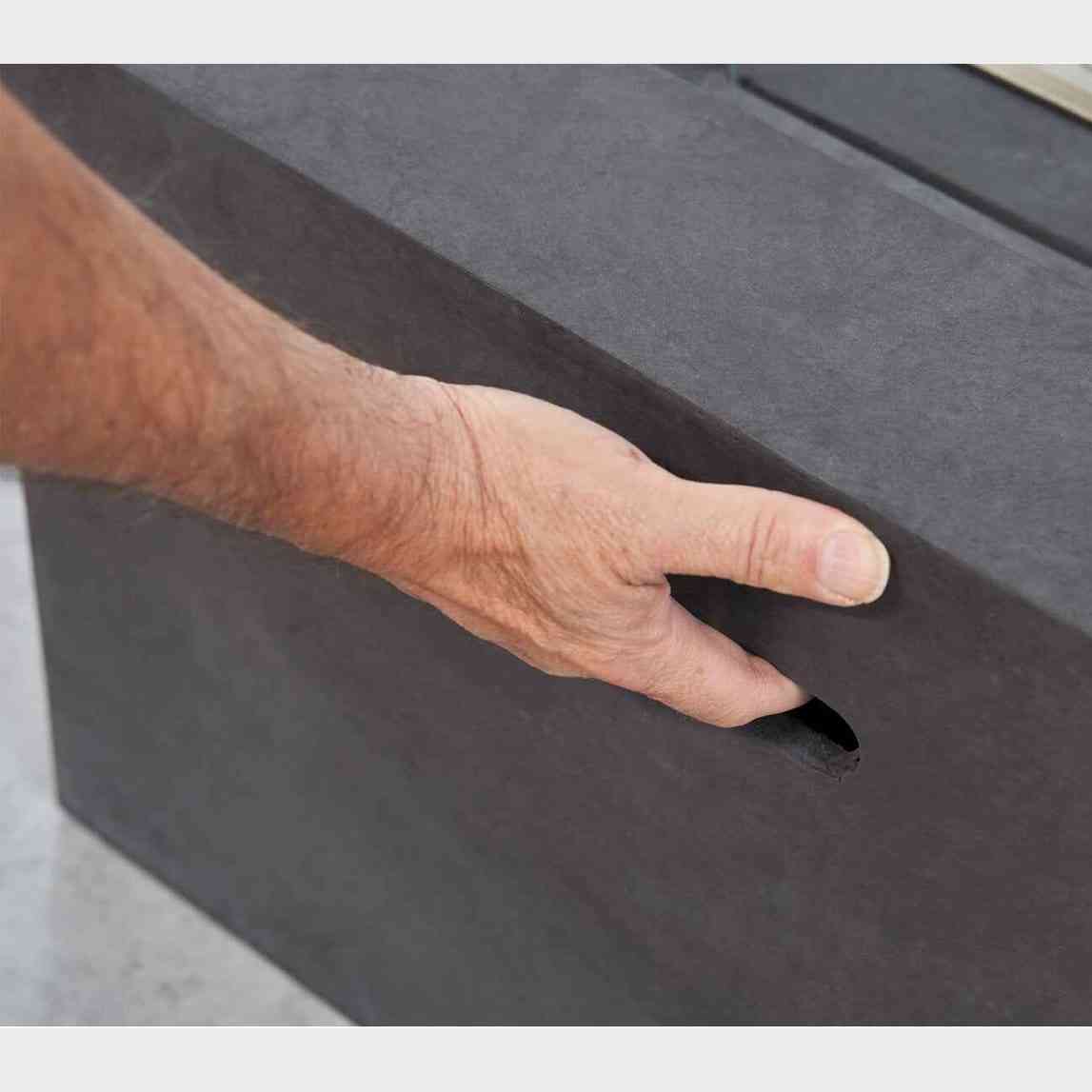 Close-up of hand gripping oval handle on matte textured dark concrete grey fire pit side