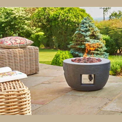 Grey gas fire pit warming stone patio with wicker furniture in garden setting