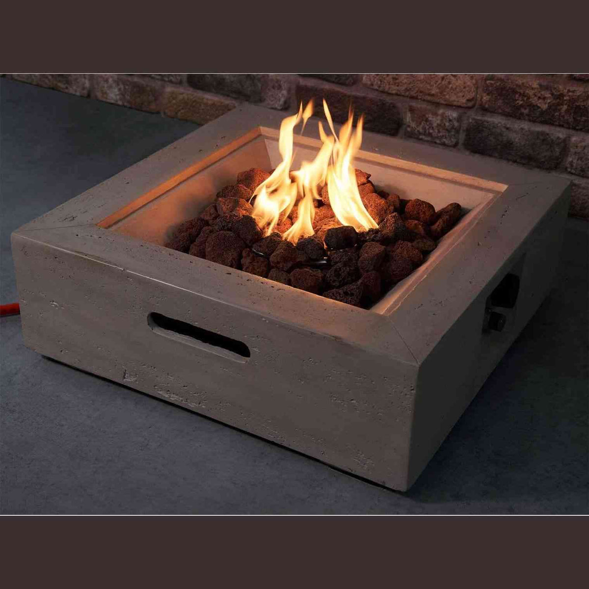 Side angle of lit square concrete fire pit with handle cutout and control knob