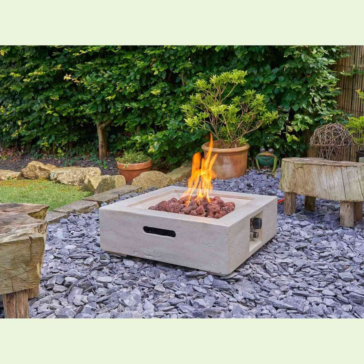 Outdoor square concrete fire pit in garden setting with orange flame