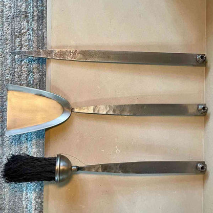 Close-up of matte forged steel fireplace tools showing weathered silver-gray finish and screw fastenings