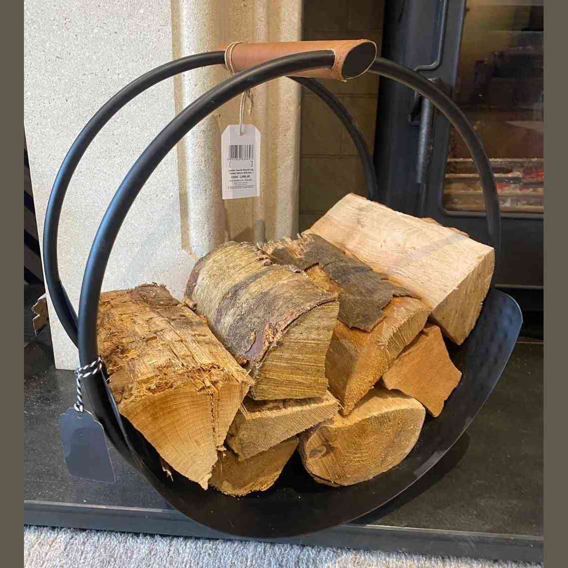 Ivyline black iron round log holder with leather handles holding firewood on stone hearth