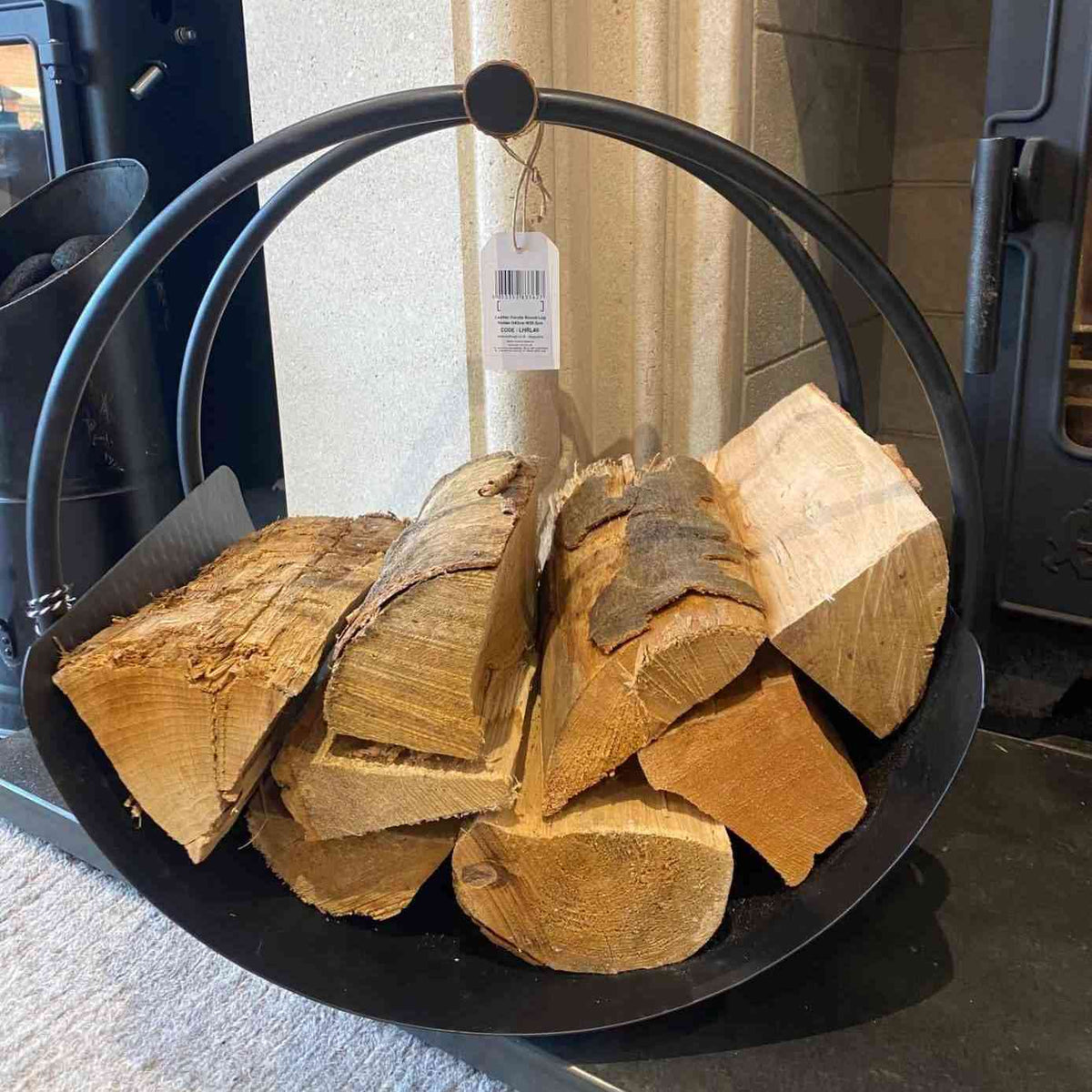 Black metal log basket with brown leather grip filled with wood against beige wall