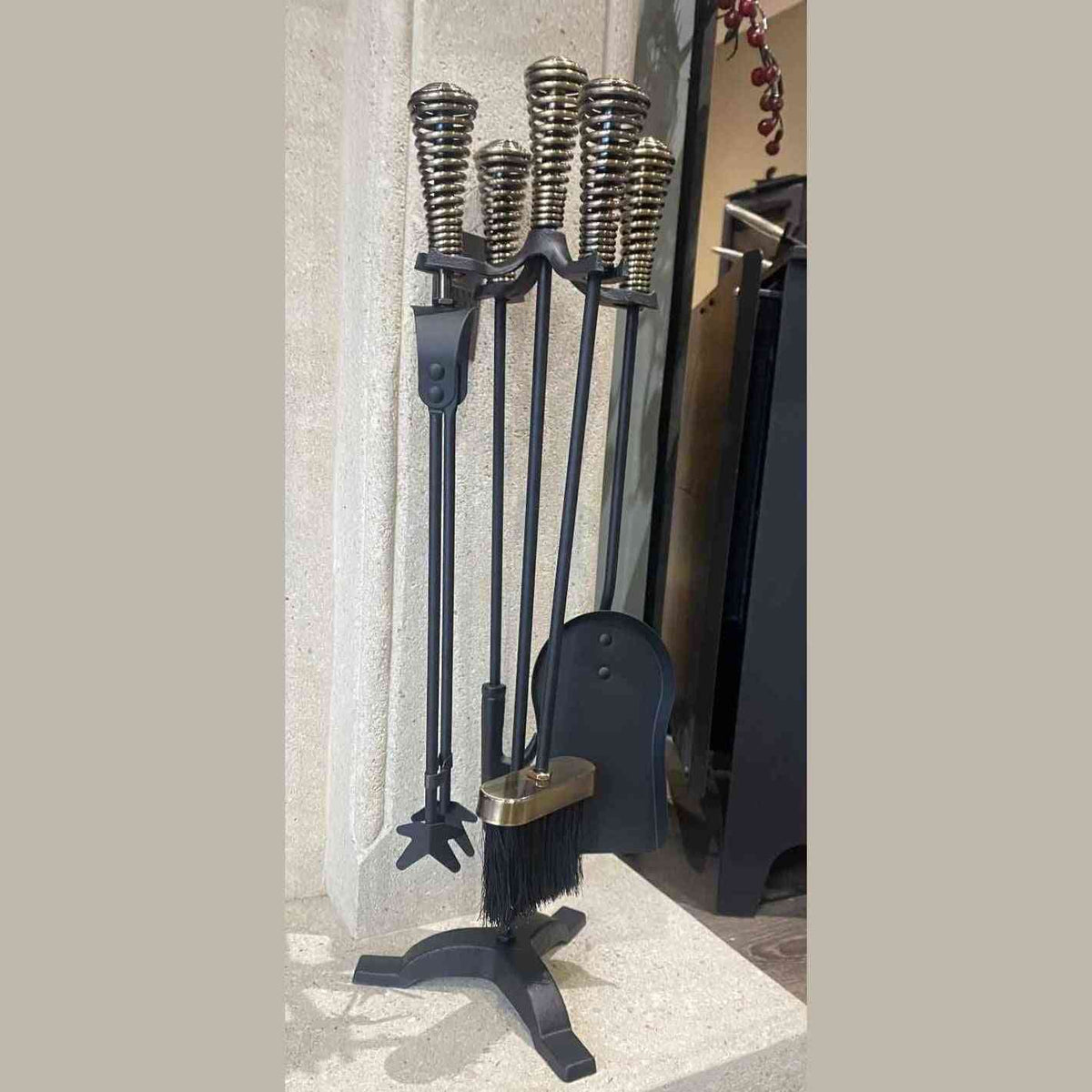Black iron fireplace tool set with tripod base, brass handles, and red berry decor