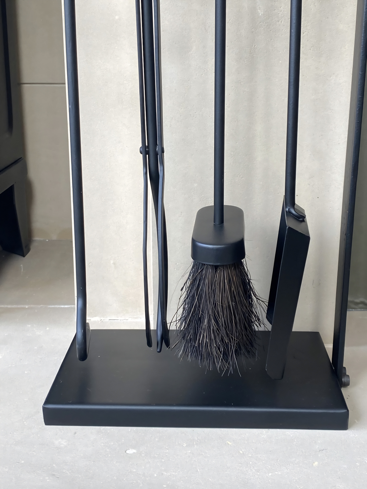Close-up view of the low-profile rectangular base and lower half of the Calfire Burlton companion set showing the black hearth brush and tools hanging neatly