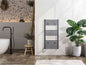 Grey electric towel radiator with digital control on a white bathroom wall, next to a large green plant in a white pot