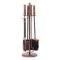 A traditional four-piece Stamford fireside companion set featuring log tongs, a fire poker, an ash shovel, and a hearth brush neatly hung on a freestanding circular base stand in a hand-finished antique copper style.