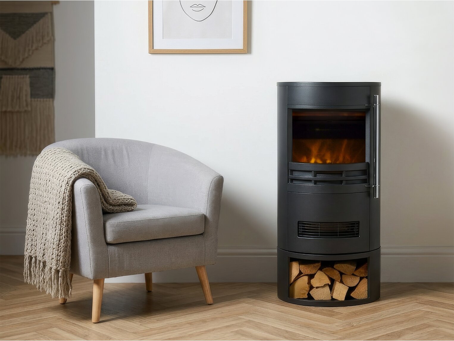 Sureflame Dunston freestanding cylindrical electric fireplace with integrated log store placed next to a grey armchair in a well-lit home interior.
