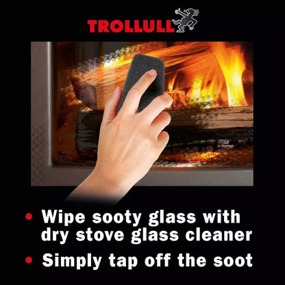 Close-up of a hand using the Trollull dry wiper pad to clean soot off a wood-burning stove glass door.